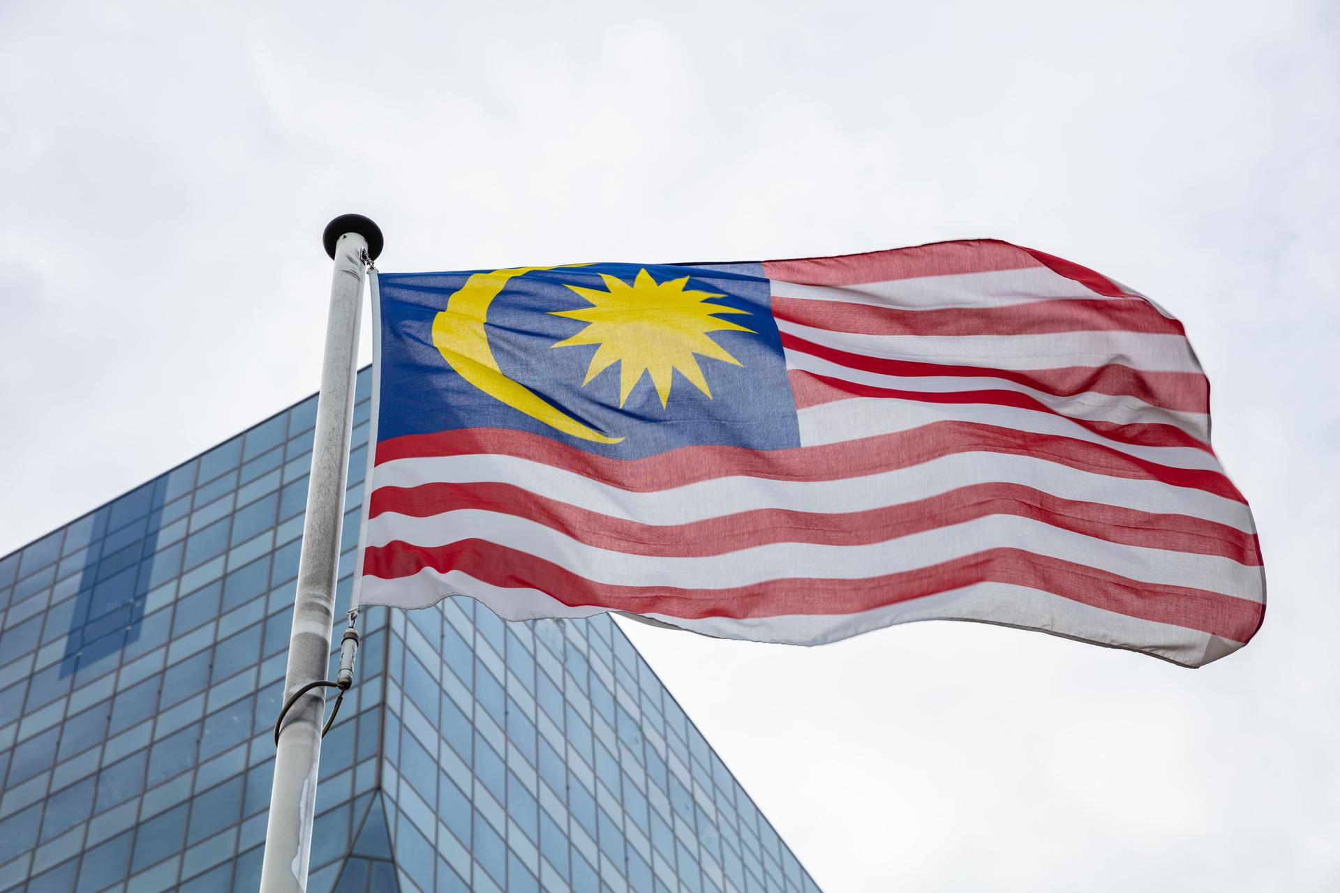 Malaysia flag on a pole waving, modern office building background